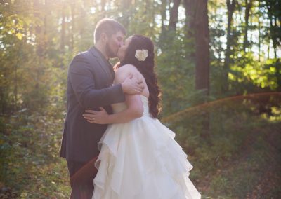Bride and groom kissing in a sun draped forest
